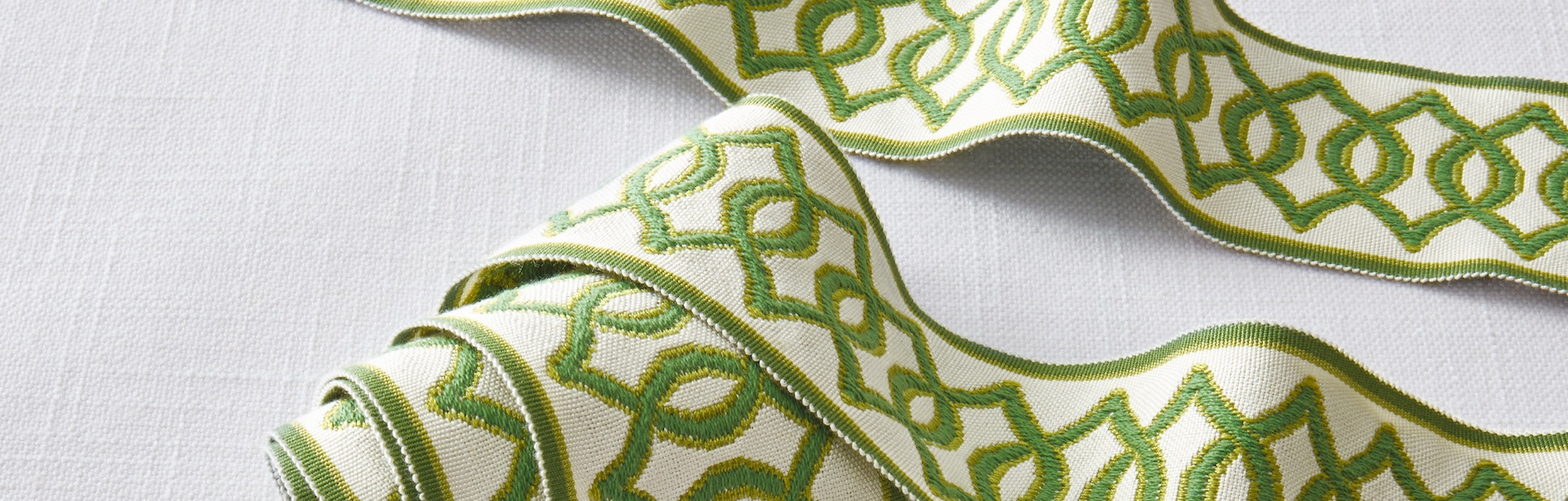 Slider images-Green Trim Detail of Paramount trimming from Carole Fabrics with a bold two-toned green pattern on a white fabric background.