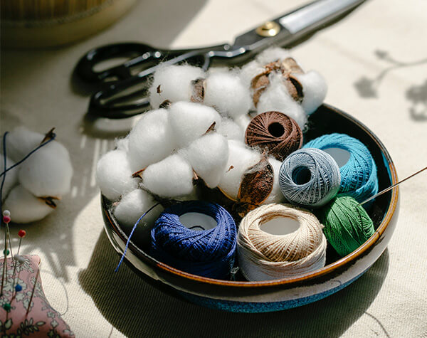 A bowl of yarn and cotton bolls on a cloth-covered surface.