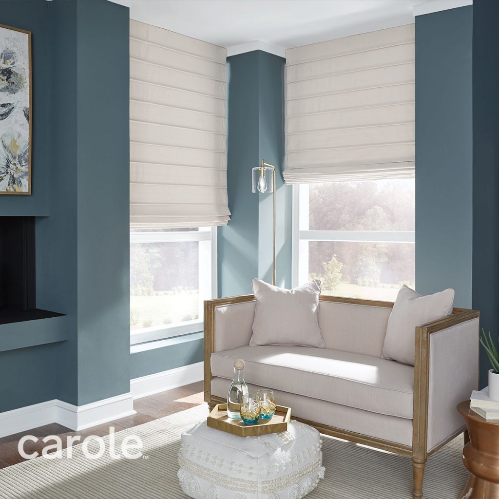 A medium blue living room with light neutral furniture and off-white Front Fold Roman Shades on the windows.