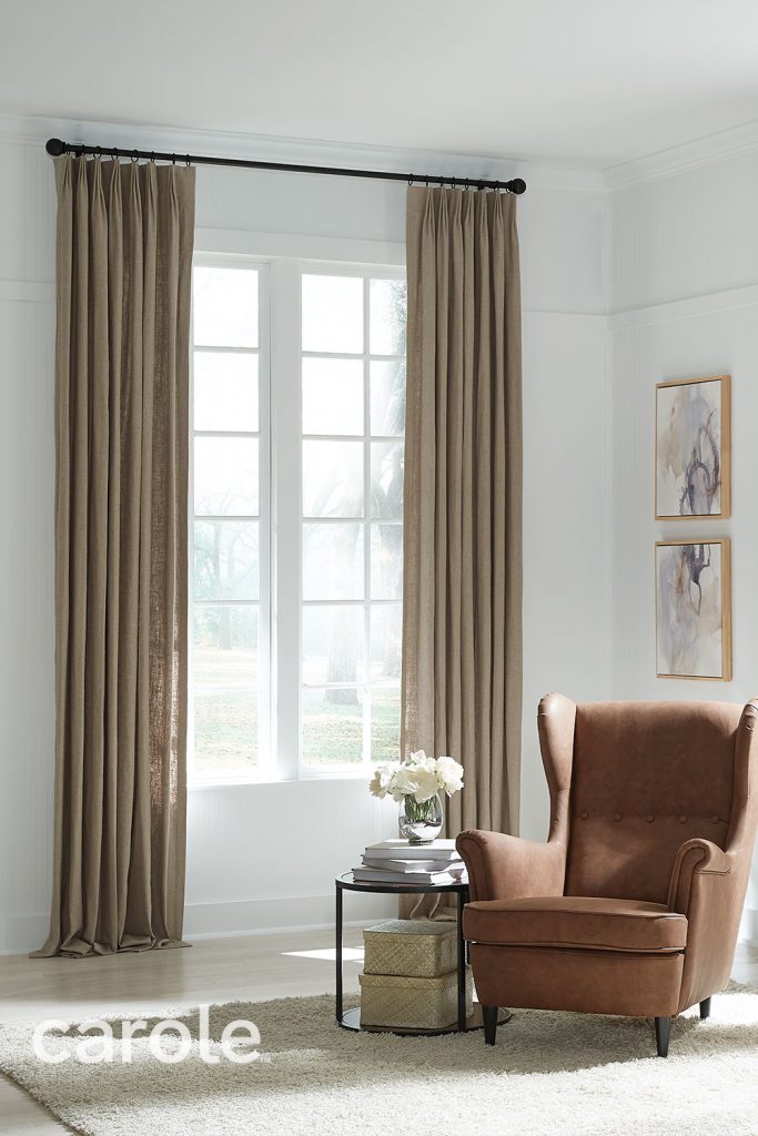 Beige Inverted Pleat Drapery in a white room with a brown leather armchair and small side table.