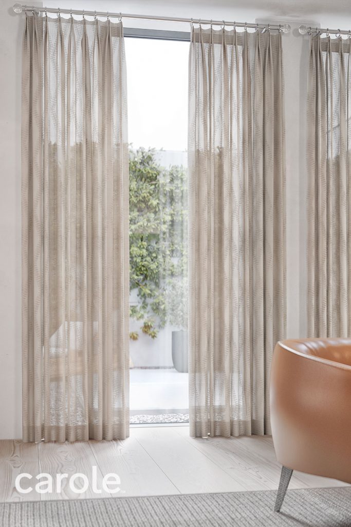 Sheer beige Olivia Pleat Drapery in a a light neutral room with a dark orange chair.