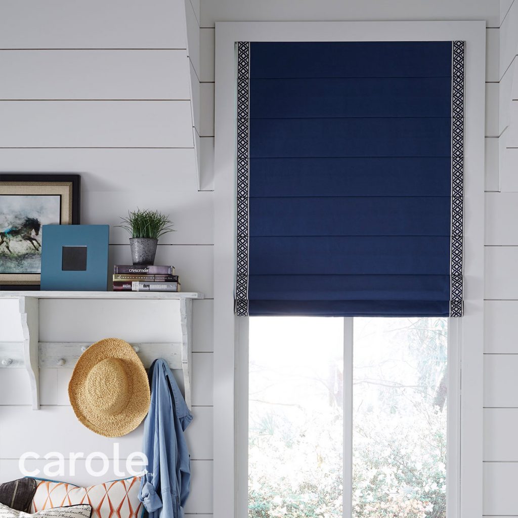 A white mudroom with a window covered in a dark blue Reverse Fold Roman Shade with Vertical Trim in a dark blue and white geometric pattern.