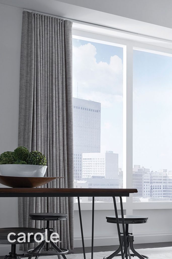 Textured solid gray Ripplefold Drapery over a large expanse of windows in a modern pale grey dining room.