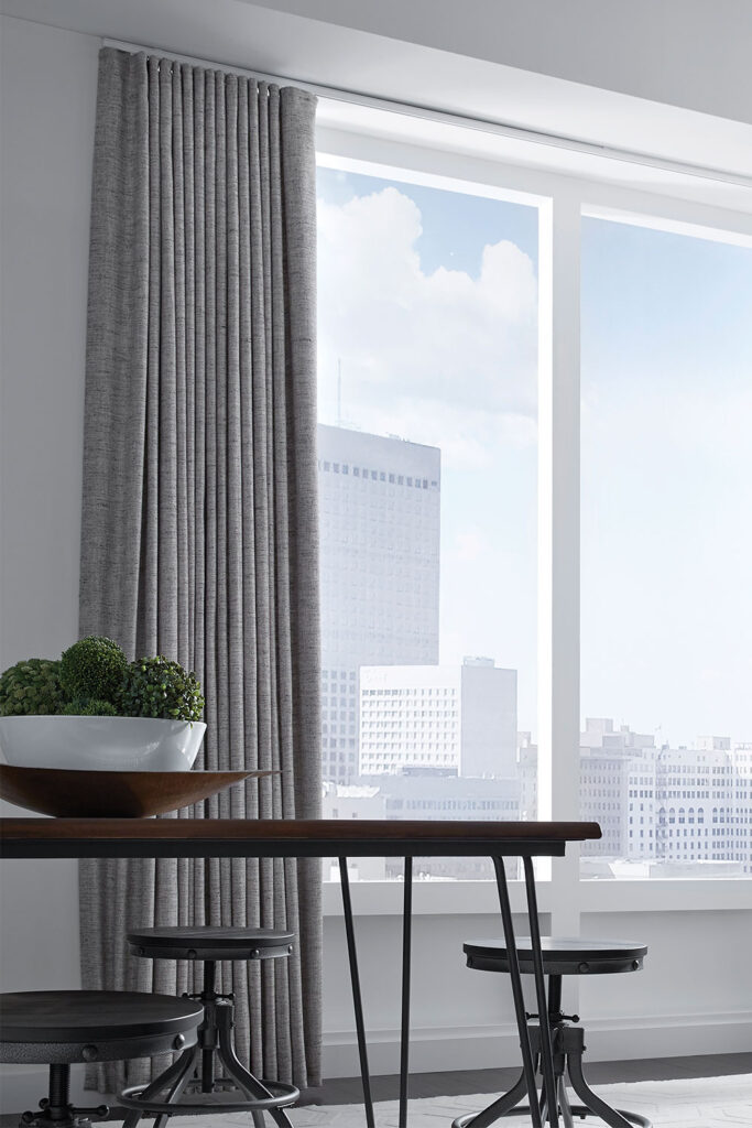 Textured solid gray Ripplefold Drapery over a large expanse of windows in a modern pale grey dining room.