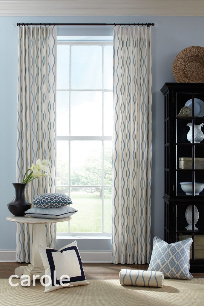 Single Pleat Drapery with light blue ripple stripes on white fabric in a pale blue room with pillows and a dark wood cabinet.