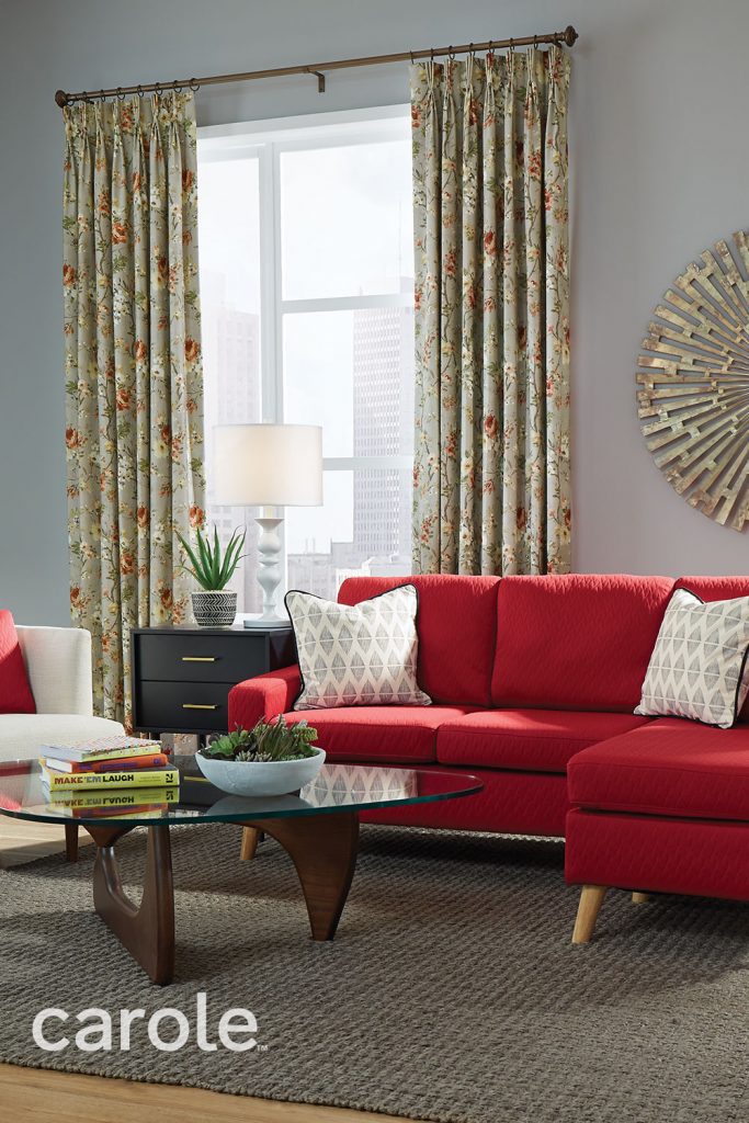 A large scale red and yellow floral pattern on sage green Three Finger Pinch Pleat Drapery in a living room with a bright red sofa.