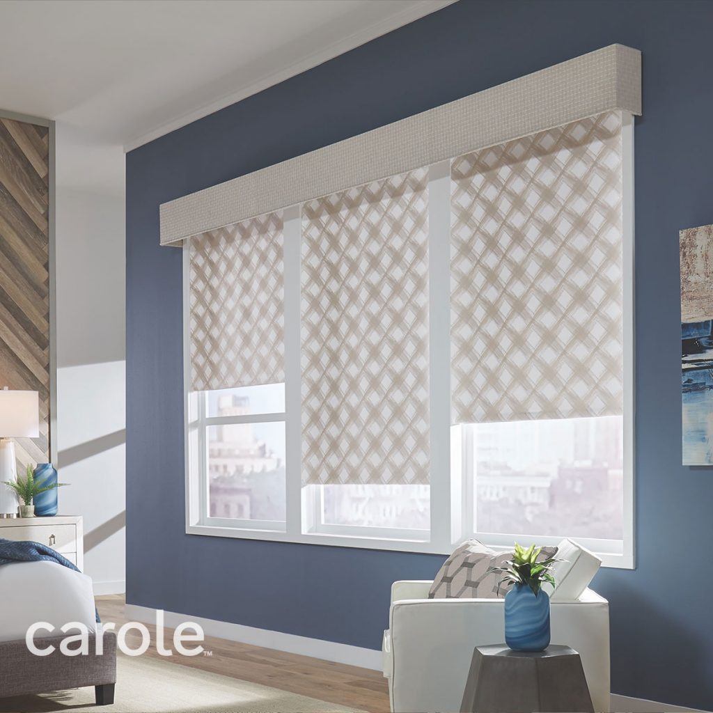 A blue-walled bedroom with a Statler Cornice top treatment in a subtle white and beige checked fabric over a panel of windows with Decorative Fabric Roller Shades in a beige and white geometric pattern.