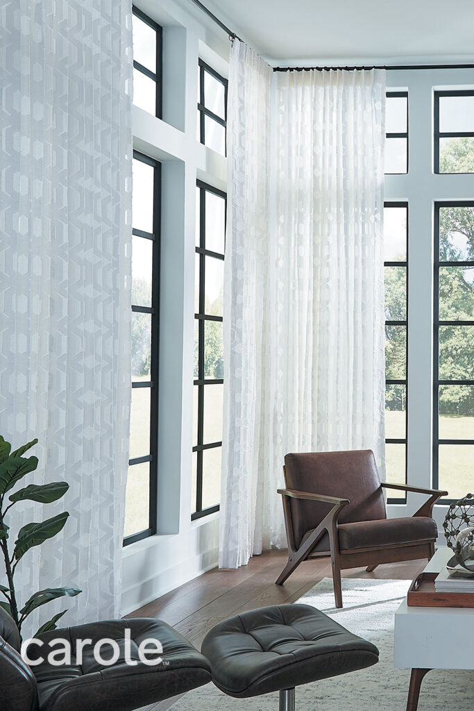 Two walls of windows that meet in the corner of a living room with floor to ceiling white sheer Single Pleat Drapery.