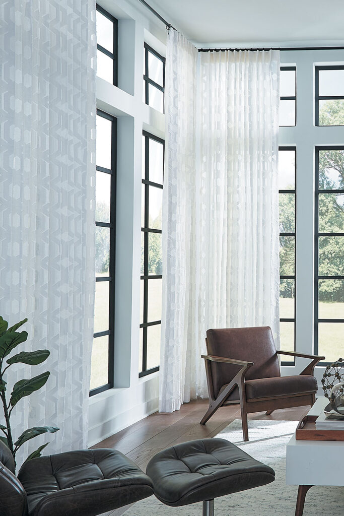 Two walls of windows that meet in the corner of a living room with floor to ceiling white sheer Single Pleat Drapery.