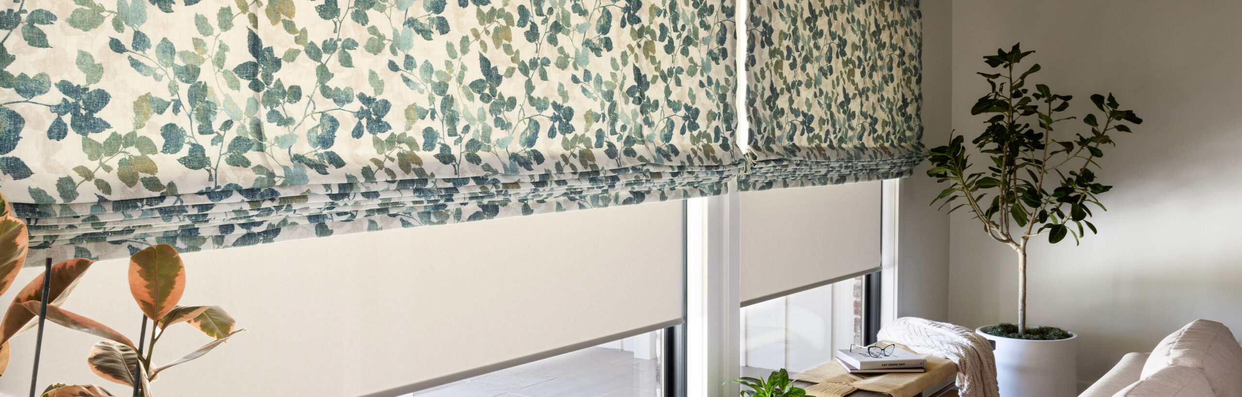 A wall of windows with PowerView Automation on soft Roman Shades with a blue and green leaf pattern.