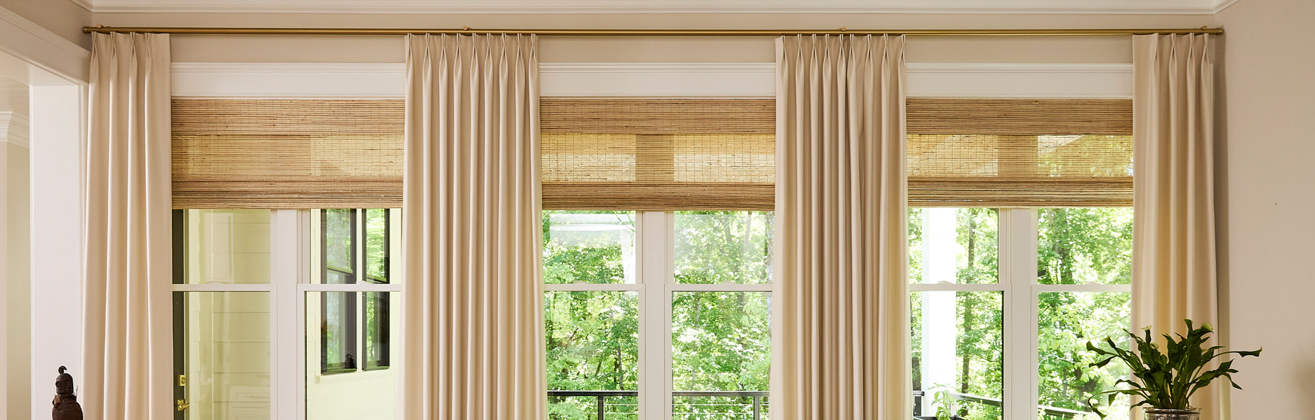 A wall of windows in a family room featuring Forest Drapery Hardware with drapery from Carole Fabrics over shades from Hunter Douglas, all in warm light neutral tones.