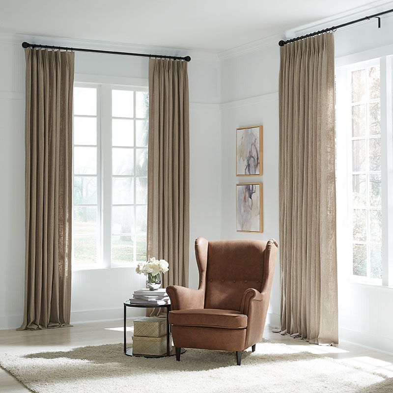 A corner of a white and neutral room featuring a brown leather chair between two windows with beige drapery in Magnolia Hardware.