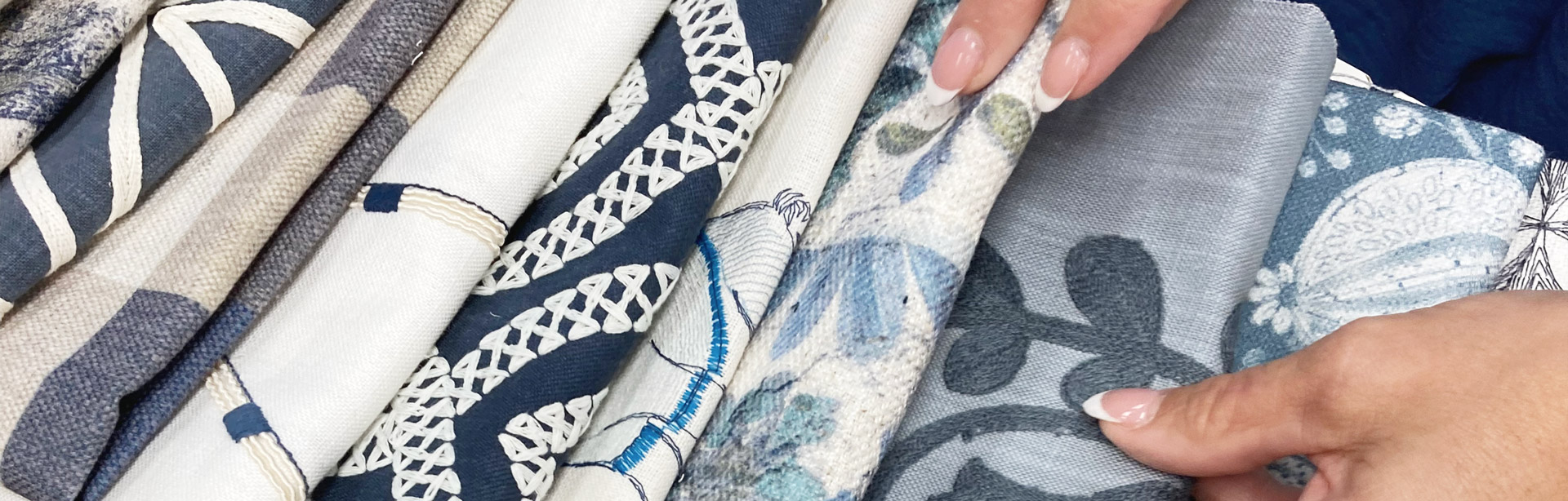 A woman's hands arranging folded patterned fabrics in a range of blues.