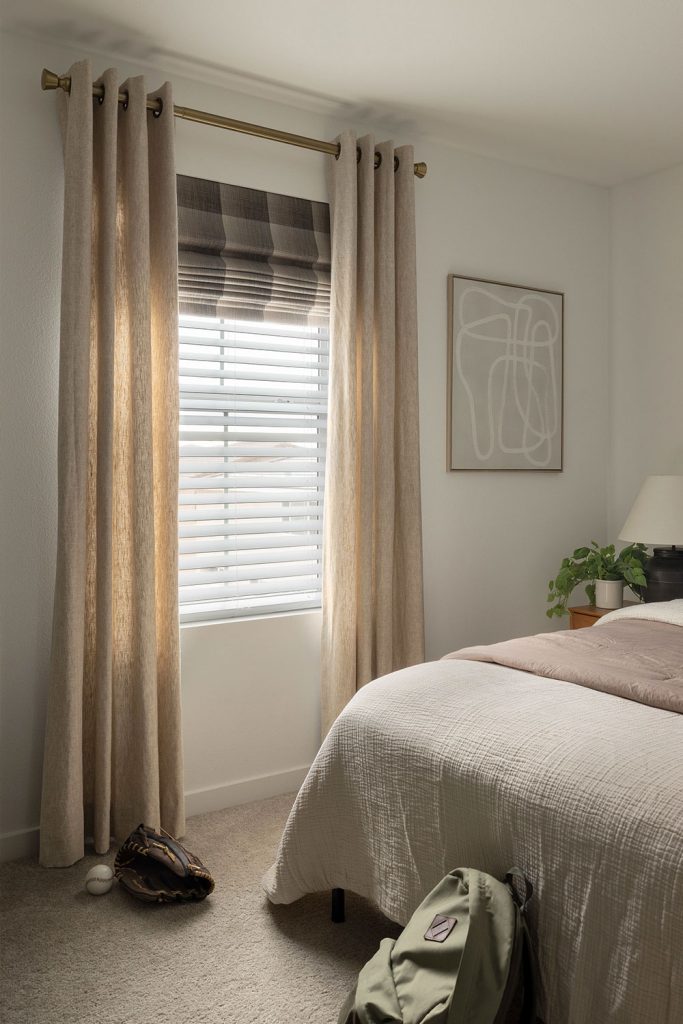 A neutral bedroom featuring EZ Panels drapery with Grommet Heading over a Flat Roman Shade.
