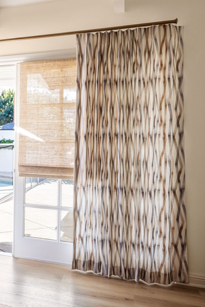 Drapery in a contemporary embroidery pattern over a set of doors in a neutral living space.