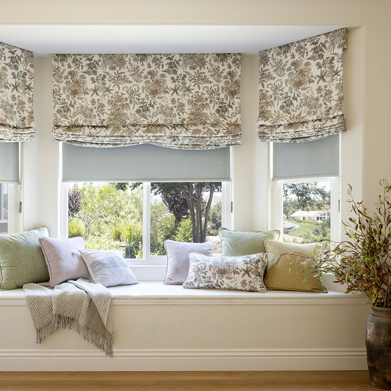 A bay window with cozy bench seating featuring Faux Soft Romans in a neutral-colored large scale floral motif.