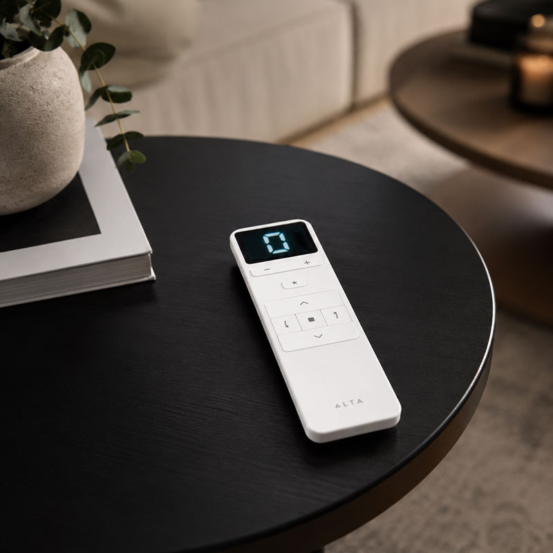 A white remote control for Alta BLISS Automation 2.0 on a dark tabletop.