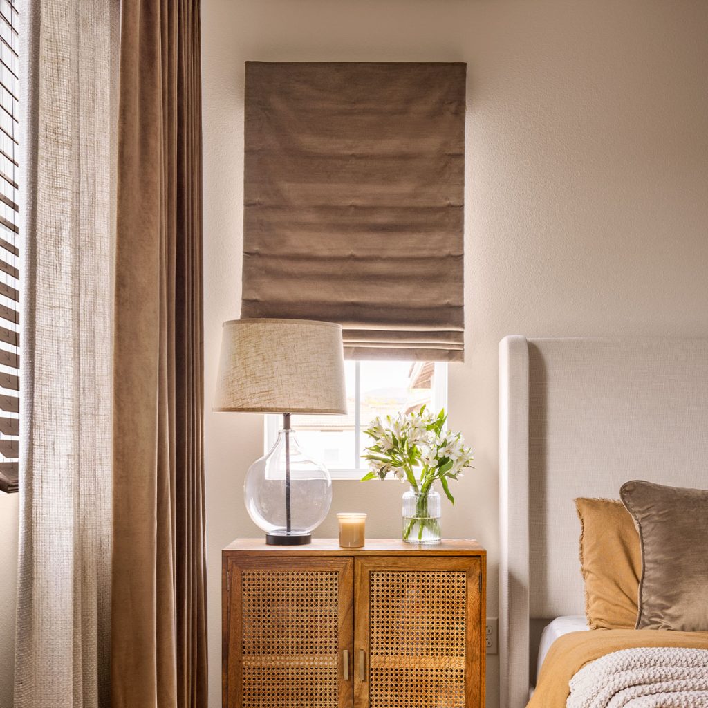 A bedroom in warm brown tones featuring a soft Flat Roman Shade on a small window over the nightstand.