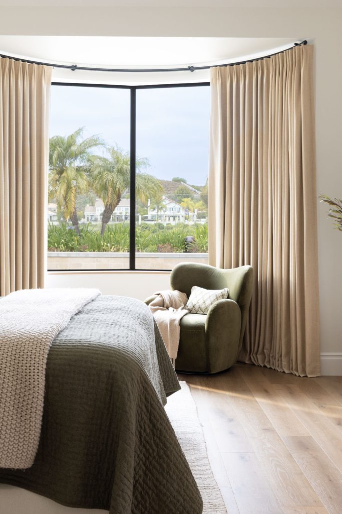 A bedroom featuring a large bowed window with neutral drapery on curved traversing drapery hardware.