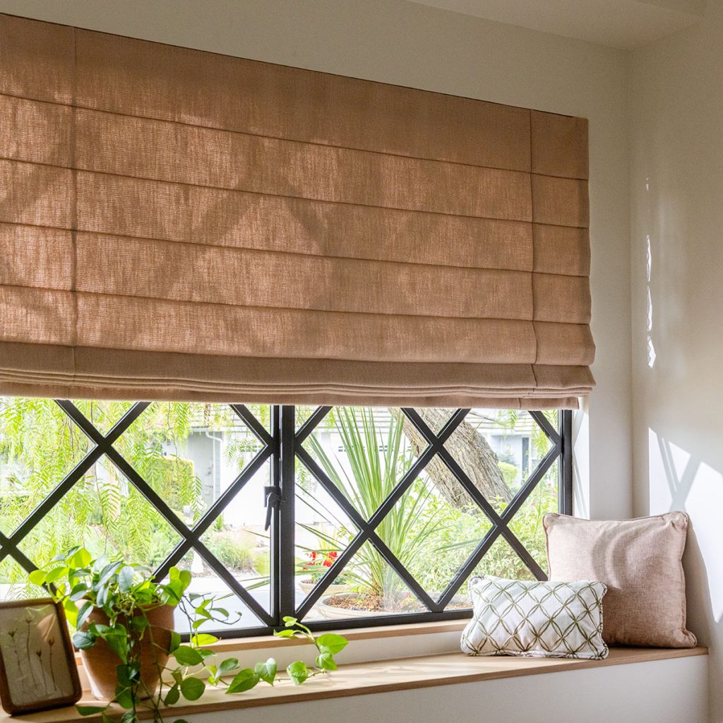 A large window over a bench seat, featuring a Reverse Fold Roman Shade in a solid mid-tone rose color.