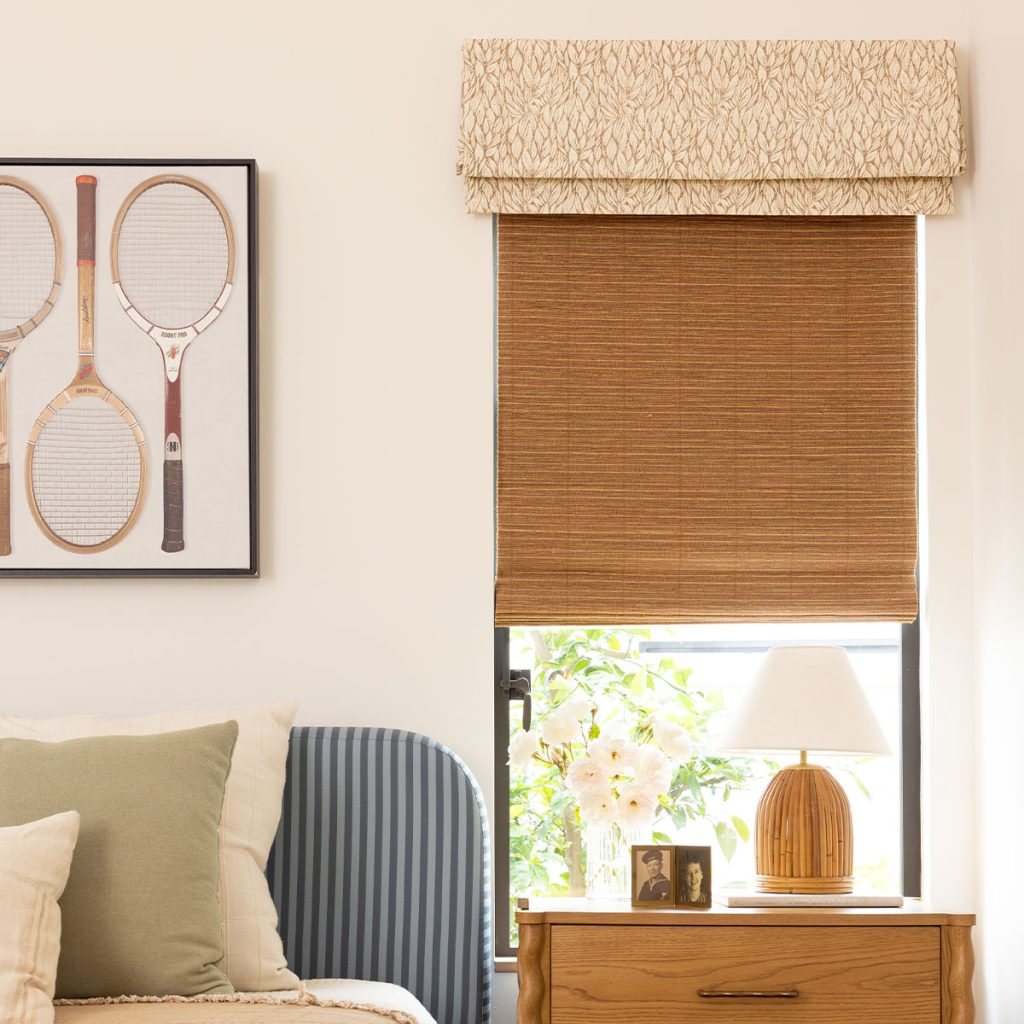 Detail of a bedroom featuring a window with a Judith Board Mounted Valance in a neutral leaf pattern over a mid-tone brown woven shade.