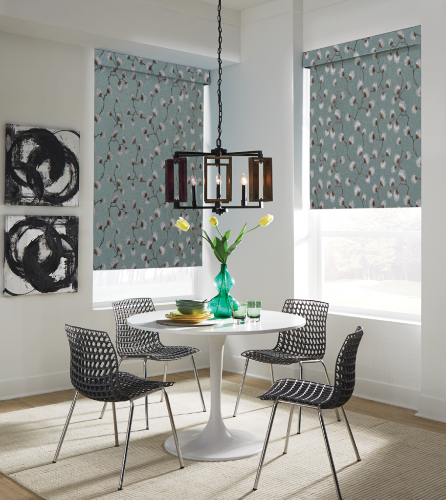 Small dining area with windows that have fabric roller shades in a floral embroidery pattern from Carole Fabrics.